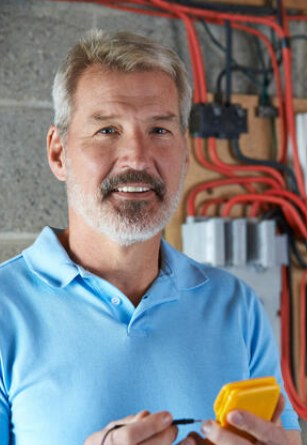 Électricien souriant avec multimètre devant un tableau électrique